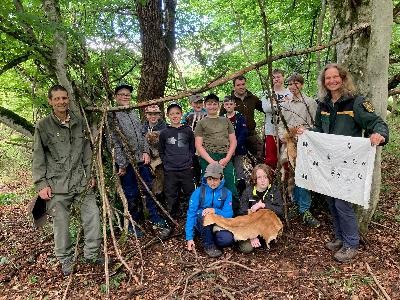 13 zufrieden wirkende Personen haben sich in einem grünenden Wald für ein Gruppenfoto positioniert