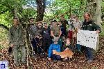 13 zufrieden wirkende Personen haben sich in einem grünenden Wald für ein Gruppenfoto positioniert